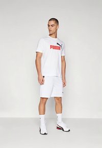 Baltas sportinis marškinėlis su raudonu „PUMA“ logotipu ir juodo katino emblemą, derinamas su baltais šortais ir baltais sportbačiais su raudonomis detalėmis.