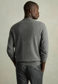 Pull en maille grise avec un col rond, des poignets et un ourlet côtelés, associé à un pantalon gris foncé. Texture subtile, design ajusté.