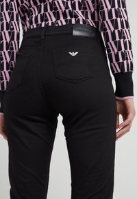 Svarta denimbyxor med smal passform, som har en läderetikett vid bakre midja, två bakfickor och en liten silverlogotyp som accent.