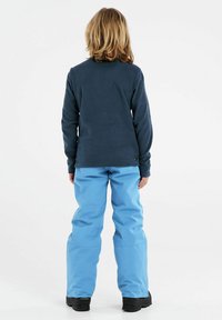 Blå fleece långärmad tröja i kombination med ljusblå vattentäta byxor, med en avslappnad passform. Svarta vinterskor fulländar outfiten.