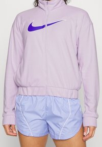 Lila vetoketjupaita, jossa on valkoinen ja violetti Nike-logo. Yhdistetty vaaleansinisiin urheilushortseihin, joissa on valkoinen reuna ja joustava vyötärö.