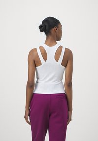 Witte geribbelde tanktop met brede schouderbanden en een uitgesneden rug, gecombineerd met paarse high-waisted broek. Gladde textuur, aansluitend ontwerp.
