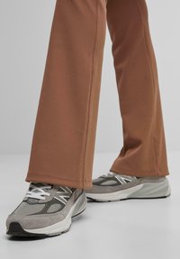 Grijze sportieve schoenen met witte veters, gemaakt van mesh en suede, gecombineerd met bruine, skinny broek met zichtbare naden en een gladde textuur.