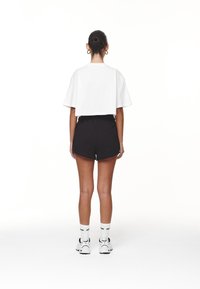 Vitt kortärmad t-shirt, svarta shorts med elastisk midja, vita strumpor med svarta accenter och vita sneakers. Modell sedd bakifrån.