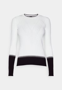 Pull côtelé à manches longues avec le haut du corps blanc et des poignets et un ourlet noirs, présentant un motif en V subtil sur la poitrine.