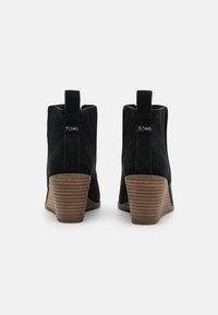 Bottines en suede noir avec un talon empilé et rainuré. Elles comportent une languette et une étiquette de marque à l'arrière. Texture lisse, design effilé.