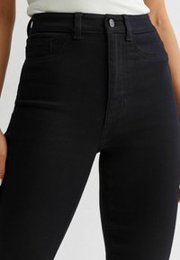 Jeans negros de tiro alto hechos de una tela suave y elástica. Incluyen bolsillos frontales, trabillas para cinturón y un diseño clásico de cinco bolsillos.