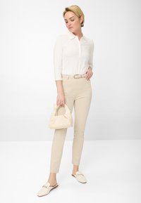 Blouse crème avec un col, pantalon beige ajusté, sac à main assorti, et chaussures légères avec un détail de bride. Tissu lisse et coupe soignée.