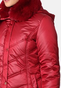 Chaqueta acolchada roja con un acabado brillante, capucha con forro de piel, diseño acolchado, botones a presión y bolsillos laterales. Estilo casual adecuado para el clima frío.