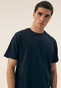 Granatowa koszulka bawełniana z krótkim rękawem, okrągłym dekoltem i luźnym fasonem, z subtelnymi detalami przeszycia wzdłuż dołu i rękawów.