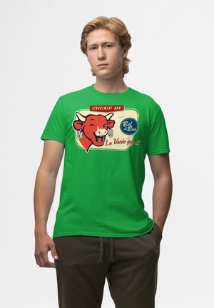 Grøn bomulds T-shirt med et rødt kuhoved med et smilende ansigt, tekst i rød og blå der står "TENDREMENT BON" og "La Vache qui rit."