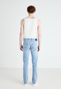 Světle modré džínové kalhoty se střihem do rovna, zadní kapsou a tmavě modrou značkovou nášivkou v pase. Stylizováno s bílým tílkem.