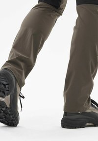 Braune Wanderhosen mit entspannter Passform und glatter Textur, kombiniert mit schwarzen und grauen Wanderstiefeln mit einer robusten Sohle.