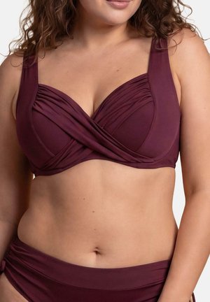 Zbliżenie kobiety noszącej bordowe bikini z szerokimi ramiączkami i skręconym wzorem materiału na górze na jednolitym tle.