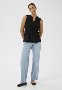Haut sans manches noir avec un décolleté en V et un motif à œillets, associé à un jean large bleu clair et des ballerines noires, offrant une coupe décontractée.