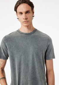 T-shirt in cotone grigio con scollo rotondo e maniche corte. Tessuto morbido con un aspetto sbiadito e usurato. Nessun modello o dettaglio visibile.
