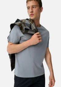 Lys grå kortærmet T-shirt lavet af blød stof, parret med en mønstret plaidskjorte draperet over skulderen, sorte bukser, afslappet pasform.