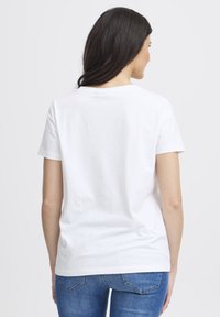 Baltas medvilninis marškinėlis su trumpomis rankovėmis, apvalia iškirpte ir vientisu nugarėle. Lygus audinys, klasikinis kirpimas, derinamas su mėlynais džinsais.