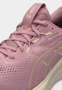 Ροζ παπούτσι για τρέξιμο ASICS GEL-CUMULUS 28 με πλέγμα στο πάνω μέρος, κορδόνια και εμφανές λογότυπο στη γλώσσα σε κοντινή λήψη.