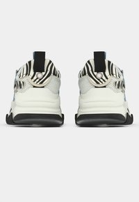 Chaussures de sport avec une tige en mesh blanc et gris, une semelle noire, un motif rayé sur le talon, et une languette pour un enfilage facile.