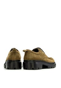 Chaussures en suede marron avec une semelle en caoutchouc noir épais, dotées d'un bout arrondi, d'un design à lacets et d'une languette à l'arrière pour un enfilage facile.