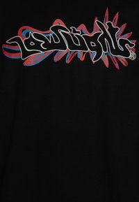 Sort t-shirt med fed, graffiti-inspireret tekst i hvid, rød og blå, med bølgede detaljer omkring bogstaverne.