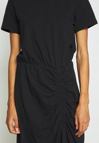 Robe noire à manches courtes avec une ceinture élastique et une texture froncée sur le côté. Confectionnée dans un tissu doux et lisse.