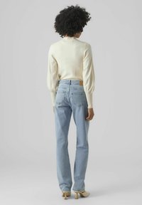 Maglione a maglia crema con maniche a sbuffo abbinato a jeans a vita alta di colore blu chiaro. Dettagli notevoli includono tasche posteriori e una toppa in pelle marrone.