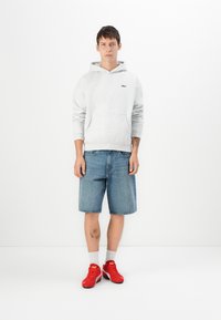 Sweatshirt cinza com capuz e bolso frontal, calções de ganga azul claro e ténis vermelhos com meias brancas. Design simples e estilo casual.