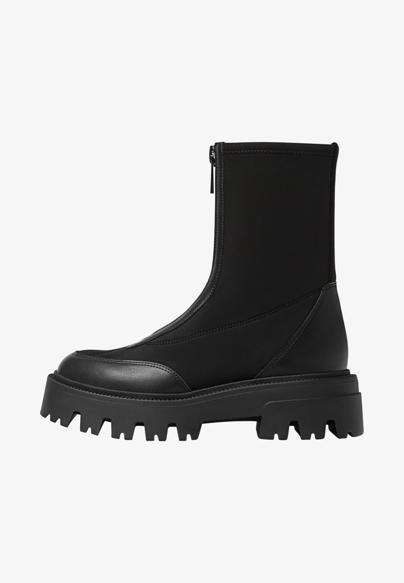 Črne gležnjarje z zadrgo, ki imajo gladek usnjen nos in teksturiran visoki dizajn. Debel in robusten gumijast podplat.