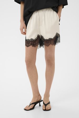 Beige shorts med sort blondekant båret af en person i sorte høje hæle sandaler og en løs sort top.