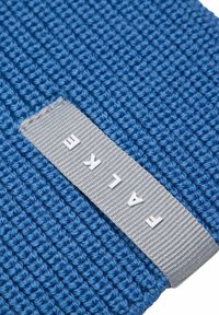 Tessuto blu texture con un motivo intrecciato, dotato di un'etichetta grigia con lettere bianche embossate che scrivono "FALKE."