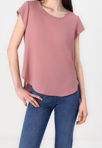 Korte mouwen, roze top van lichtgewicht stof, met een ronde halslijn en een gebogen zoom. Gecombineerd met blauwe denim jeans.