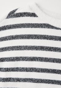 Svetrový černobílý pruh s jemnou, texturovanou látkou, která má střídající se široké a úzké pruhy a kulatý výstřih.