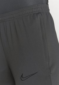 Mørkegrå træningsbukser med elastisk linning, sidelommer og et sort Nike-logo broderet på fronten. Glat stofstruktur.