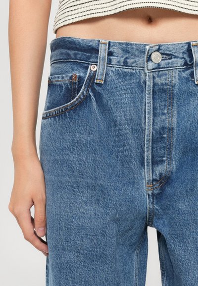 Faded blue denim jeans with a high waist, five pockets, and orange stitching accents. Features a silver button closure at the waist.