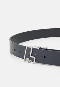 Cinto em couro cinza escuro com textura lisa e acessórios em prata. Apresenta uma fivela retangular com um "L" e um detalhe de logotipo de crocodilo.
