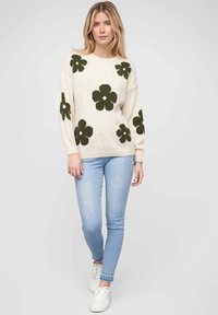 Cream sweater with large dark green flowers; ribbed cuffs and hem. Paired with light blue jeans and white sneakers. Simple, casual design.