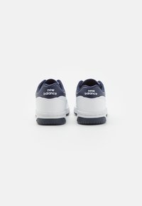Białe i granatowe sneakersy z gładką skórzaną cholewką, amortyzowanym obcasem, gumową podeszwą i logo "new balance" na zakładce pięty.