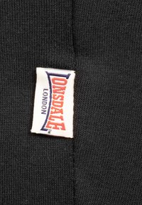Zwarte stof met een ribbelstructuur, voorzien van een Lonsdale London label in het wit met rode en blauwe letters.