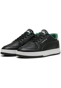 Black leather sneakers with green accents, white rubber sole, perforated toe, and black laces. Features logo on tongue and side.
