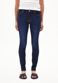 Jeans skinny en denim bleu foncé avec un design classique à cinq poches, des détails de couture subtils et une texture lisse et extensible.