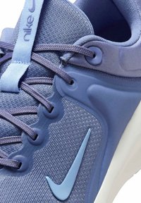 Zapatilla Nike con una parte superior de malla texturizada en un tono púrpura claro, acentos flexibles en azul y un logotipo swoosh prominente en azul a juego.