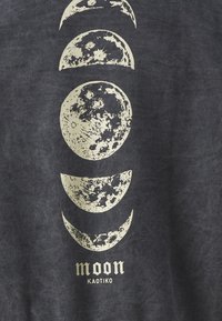 T-shirt grigio scuro con fasi lunari stampate in bianco sporco, con una texture vintage. Sotto il design ci sono le scritte "moon" e "KAOTIKO".