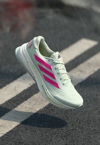 Jasnozielony but sportowy z różowymi paskami, teksturowana siateczka, wyściełany kołnierz, odblaskowe akcenty i opływowy design.