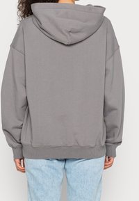 Hellgrauer Hoodie mit großer, verstellbarer Kapuze, abfallenden Schultern und gerippten Bündchen. Weiches Baumwollmischgewebe, entspannte Passform.