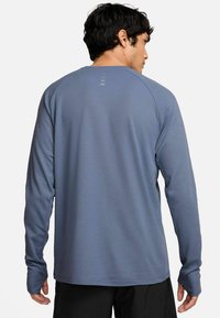 Langärmliges Sportshirt in Hellblau, hergestellt aus feuchtigkeitsableitendem Material. Mit Raglanärmeln und Daumenlöchern an den Bündchen.