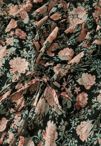 Tissu noir avec un motif floral rose et vert, un nœud noué et de doux volants créant des plis texturés.