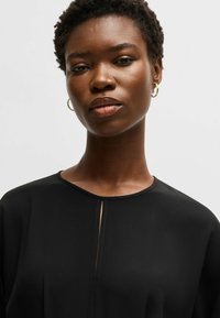 Svart topp med rund halsringning, kort ärm och en centralt vertikalt skär detalj, gjord av ett mjukt, lätt tyg.