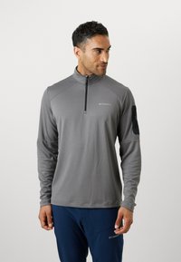 Grå langermet genser med kvart-zip krage, laget av lett stoff. Har et logo på brystet og en glidelåslomme på ermet.
